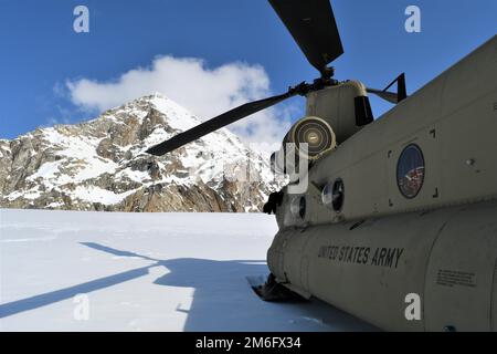 Auf dem Kahiltna-Gletscher parkt ein CH-47F-Chinook-Hubschrauber, während die Soldaten der Bravo Company, des 1. Bataillons, des 52. Luftfahrtregiments, auch bekannt als Sugar Bears, die Ausrüstung für den National Park Service im Bergsteigerbasislager entladen. (FOTO DER US-Armee, Eve Baker, Fort Wainwright Public Affairs Office) Stockfoto