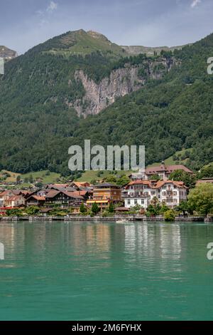 Brienzersee, Brienzersee mit türkisfarbenem Wasser - traditionelle Holzhäuser in der Nähe von Interlaken mit Schweizer Alpen im Hintergrund, Stockfoto