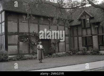 1950er, historisch, eine Dame, die auf einer Rasenfläche hinter William Shakespeares Geburtsort steht, einem Fachwerkhaus aus dem 16. Jahrhundert in Henley Street, Stratford-upon-Avon, England, Großbritannien. Das alte Haus wurde 1847 vom Shakespeare Birthplace Trust gekauft. Stockfoto