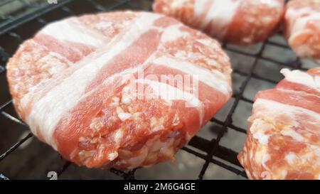 Rohe Fleischschnitzel, die in Speck eingewickelt sind, werden auf dem Grillregal gekocht. Der Koch bereitet die gegrillten Burgerpasteten zu. Zutaten für ma Stockfoto