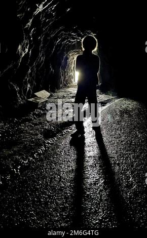 Ein Junge in einer dunklen Höhle mit Licht vom Eingang Stockfoto