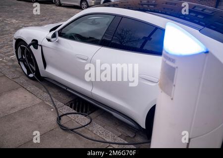 Elektroauto Porsche an einer elektrischen Ladestation in Wapping am 3. Dezember 2022 in London, Vereinigtes Königreich. Ein Elektroauto ist ein Fahrzeug, das von einem oder mehreren Elektromotoren angetrieben wird, wobei elektrische Energie in wiederaufladbaren Batterien oder einem anderen Energiespeicher gespeichert wird. Der daraus resultierende Rückgang schädlicher Emissionen macht umweltfreundliche Autos zu einer umweltfreundlichen Alternative zu Fahrzeugen mit normalem Kraftstoffverbrauch. Stockfoto