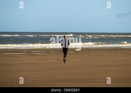 Rückansicht eines weißen männlichen Läufers am Strand von Cayton Bay in North Yorkshire, Großbritannien. Stockfoto