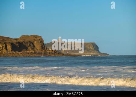 Yons NAB und Scarborough Castle vom Strand in Cayton Bay aus gesehen, mit der Nordsee im Vordergrund. Stockfoto