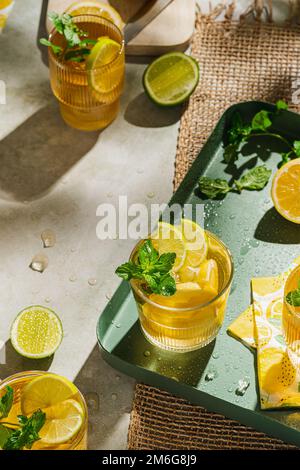 Traditioneller hausgemachter Eistee mit Zitrone, Minze und Eis in Gläsern. Sommerliches kaltes Getränk auf grünem Hintergrund. Gesundes Sommeressen Konzept. Selektiver Fokus Stockfoto