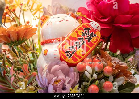 Chinesische Neujahrsdekoration mit Maneki-Neko oder Glückskatze. Das Wort auf dem Nummernschild bedeutet Geld. Chinesisches Neujahrskonzept. Stockfoto