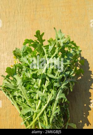 Ein Haufen frischer grüner Rucola auf hellem Holzhintergrund, helles Sonnenlicht, Draufsicht, flach Stockfoto