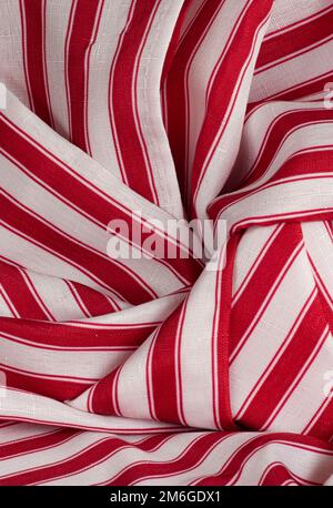 Sehen Sie eine Nahaufnahme aus rot-weißem Streifenmaterial in Rollen, Kurven und Falten. Dimensionales Hintergrundmaterial mit Textur ist horizontal oder vertikal zu sehen. Stockfoto