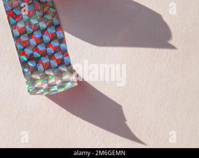 Ein Stück holographische Folie auf weißem Hintergrund, harte Schatten von der Folie. Draufsicht. Zu kopierende Position Stockfoto