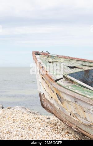 Ein altes Holzboot mit abblätternder Farbe an einem Sandstrand mit Wasser im Hintergrund. Stockfoto