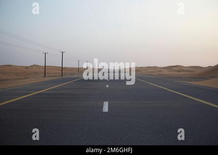 Sand bläst über einen verlassenen, geraden Wüstenautobahn, während er sich bis in die Ferne erstreckt Stockfoto