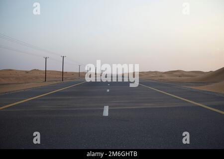 Sand bläst über einen verlassenen, geraden Wüstenautobahn, während er sich bis in die Ferne erstreckt Stockfoto