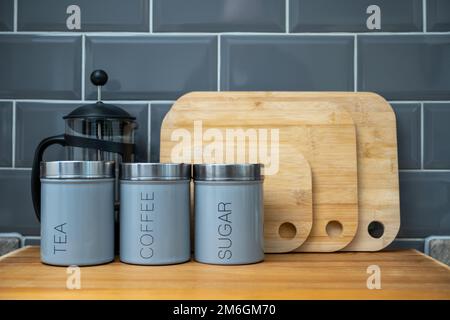 Kaffee, Tee und Zucker luftdichte Kanister Glas Cafetiere mit Bambus Schneidebrettern in der Küche vor grauem Fliesenhintergrund Stockfoto