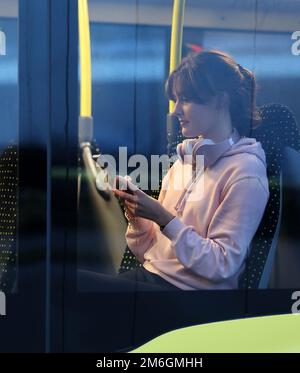 Parchim, Deutschland. 04. Januar 2023. Auf einer Presseveranstaltung der öffentlichen Verkehrsgesellschaft Ludwigslust-Parchim, um das kostenlose WLAN in Bussen zu präsentieren, sitzt Marie Wolf, eine Mitarbeiterin, mit einem Handy in einem Bus. Alle elektrischen Busse, die von der öffentlichen Verkehrsgesellschaft betrieben werden, müssen mit dem kostenlosen WLAN ausgestattet sein. Kredit: Bernd Wüstneck/dpa/Alamy Live News Stockfoto