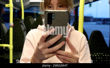 Parchim, Deutschland. 04. Januar 2023. Auf einer Presseveranstaltung der Verkehrsbetriebe Ludwigslust-Parchim zur Präsentation des kostenlosen WLAN in Bussen hält Marie Wolf, eine Mitarbeiterin, ein Mobiltelefon in einem Bus. Alle elektrischen Busse, die von der öffentlichen Verkehrsgesellschaft betrieben werden, müssen mit dem kostenlosen WLAN ausgestattet sein. Kredit: Bernd Wüstneck/dpa/Alamy Live News Stockfoto