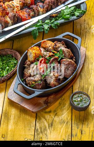 Grillfleisch - Schweinefleisch, Huhn und Gemüse auf einer gusseisernen Pfanne. Gegrillte Spieße auf gelbem Holzhintergrund. Draufsicht. Stockfoto