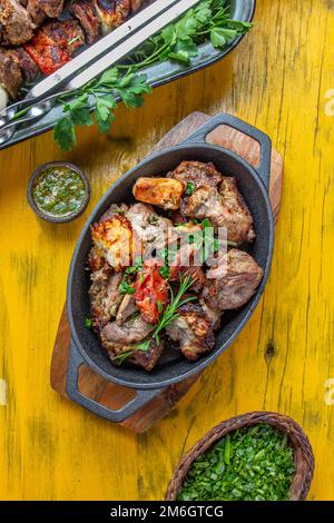 Grillfleisch - Schweinefleisch, Huhn und Gemüse auf einer gusseisernen Pfanne. Gegrillte Spieße auf gelbem Holzhintergrund. Draufsicht. Stockfoto