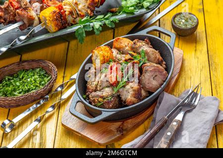 Grillfleisch - Schweinefleisch, Huhn und Gemüse auf einer gusseisernen Pfanne. Gegrillte Spieße auf gelbem Holzhintergrund. Draufsicht. Stockfoto