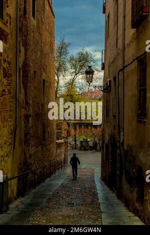 Ein Mann, der eine Gasse in Segovia entlang läuft, mit dem ersten Morgengrauen in der Ferne. Stockfoto