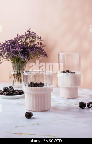 Joghurt mit Beeren in einem Glas auf hellrosa Hintergrund Stockfoto