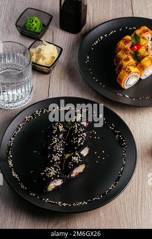 Verschiedene Arten von Sushi-Rollen in Tellern auf dem Tisch. sojasoße, Stockfoto