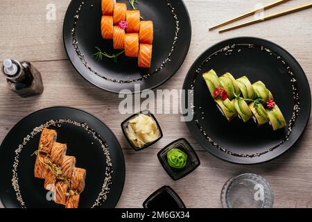 Verschiedene Arten von Sushi-Rollen in Tellern auf dem Tisch. sojasoße, Stockfoto