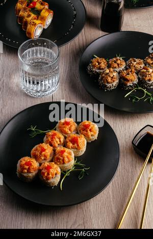 Verschiedene Arten von Sushi-Rollen in Tellern auf dem Tisch. sojasoße, Stockfoto