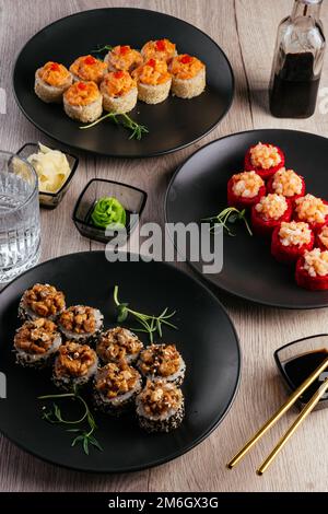 Verschiedene Arten von Sushi-Rollen in Tellern auf dem Tisch. sojasoße, Stockfoto