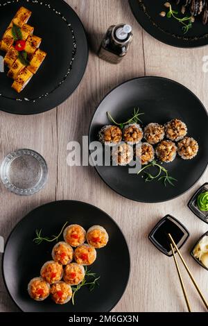 Verschiedene Arten von Sushi-Rollen in Tellern auf dem Tisch. sojasoße, Stockfoto