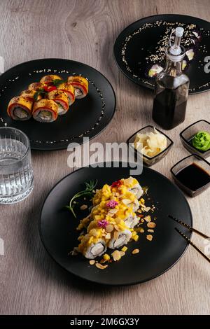 Verschiedene Arten von Sushi-Rollen in Tellern auf dem Tisch. sojasoße, Stockfoto