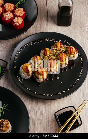 Verschiedene Arten von Sushi-Rollen in Tellern auf dem Tisch. sojasoße, Stockfoto