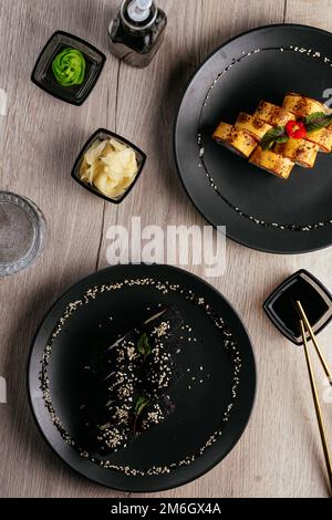 Verschiedene Arten von Sushi-Rollen in Tellern auf dem Tisch. sojasoße, Stockfoto