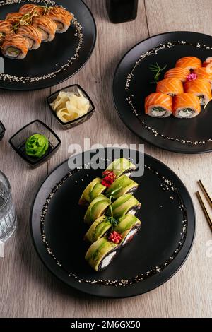 Verschiedene Arten von Sushi-Rollen in Tellern auf dem Tisch. sojasoße, Stockfoto
