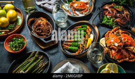 Tisch mit Meeresfrüchtegerichten - gekochte Krabben, Tigergarnelen, gegrillte Tintenfische und Tintenfische auf gusseisernen gegrillten Pfannen und Tellern, Weißwein. Draufsicht. Stockfoto