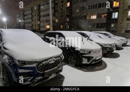 Schneebedeckte Autos, die hintereinander auf einem offenen Parkplatz im Hof geparkt wurden Stockfoto