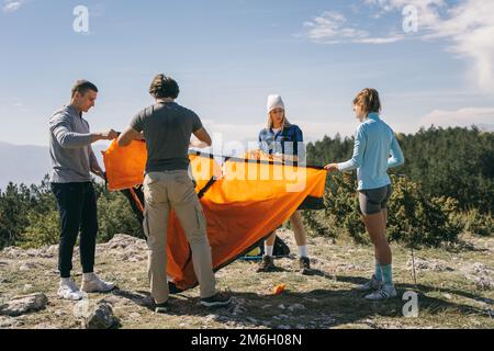 Gruppe von Wanderer, die das orangefarbene Zelt auf dem Gipfel des Berges machen Stockfoto