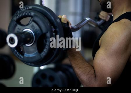 Kräftiger Muskelmann, der in einem Fitnesscenter trainiert und Gewichtheben kann Stockfoto