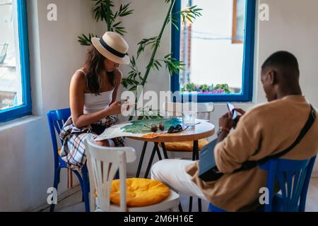 Ein schwarzer Mann und eine weiße Frau sitzen in einer Kaffeebar. Sie chatten über ihre Telefone Stockfoto