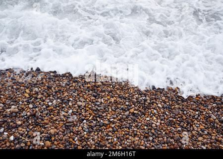 Aus nächster Nähe, wenn die schäumende Brandung über einen Strand für Menschen an der englischen Südküste angespült wird Stockfoto