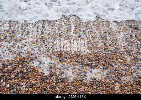 Aus nächster Nähe, wenn die schäumende Brandung über einen Strand für Menschen an der englischen Südküste angespült wird Stockfoto