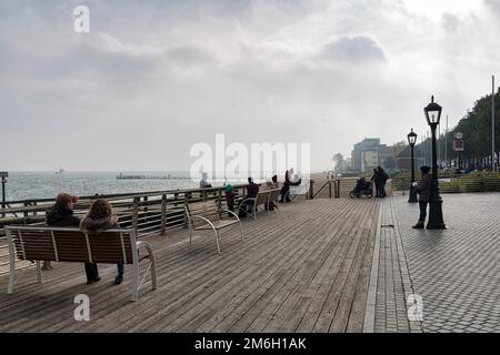 Fußgänger sitzen auf Bänken, blicken auf das Meer, düsteres Herbstwetter, Dunst, Wyk auf Foehr Promenade, Foehr Insel, Nordfriesien, Nordsee Stockfoto