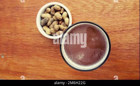 Rotes Craft-Bier mit Erdnüssen auf Holztisch Stockfoto