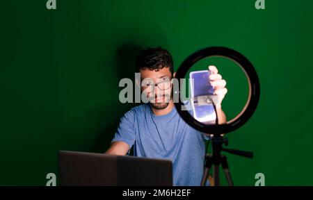 Ein Typ, der von zu Hause aus arbeitet. Konzept für Online-Kurse. Ein Mann, der Online-Kurse mit dem Telefon gibt. Ein Typ mit Laptop macht Video-Blog am Telefon. Stockfoto