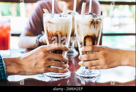 Mann und Frau, die Hand toasten und zwei Milchshake halten. Zwei Hände Toasten mit Milchshake in einem Café, Nahaufnahme von zwei Händen Toasten mit Eiskaffee Stockfoto