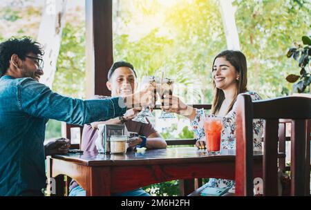 Glückliche junge Freunde, die in einem Café anstoßen. Glückliche Freunde genießen einen Milchshake in einem Café. Drei glückliche beste Freunde treffen sich und stoßen an Stockfoto
