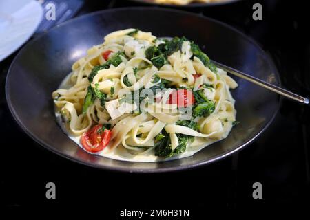 Tagliatelle mit Spinat und Cocktailtomaten, Nudelgericht, Sommerküche, Fetakäse, schwarzer Teller, Gemüse, Vegetarier, Lebensmittelfotografie Stockfoto