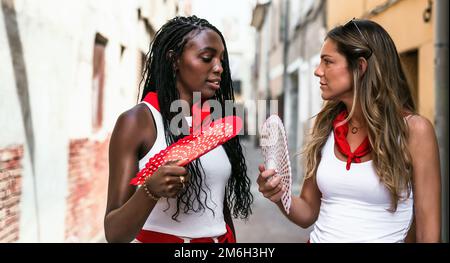 Zwei junge weiße und schwarze Freunde unterhalten sich auf der Straße mit einer gewissen Intimität während der Festlichkeiten einer Stadt in spanien. Freundschaftsbegriff, Stockfoto