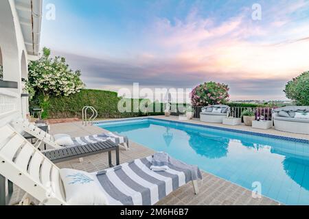 Ein Paar komfortable Liegestühle, die einen Swimmingpool umgeben, während der Sonnenuntergang entlang der Costa del Sol aus nächster Nähe Stockfoto