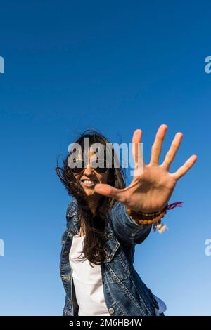 Niedrige Blickwinkel einer Frau, die sich ähnelt, während sie ihre Handfläche zeigt. Blauer Himmelshintergrund. Stoppen Sie die Geste Stockfoto