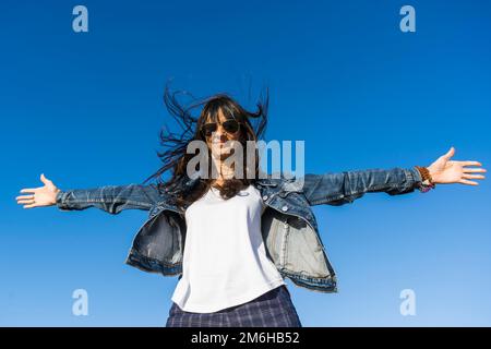 Blick aus dem niedrigen Winkel auf eine Frau, die sich ähnelt, mit offenen Armen im Freien. Blauer Himmelshintergrund Stockfoto